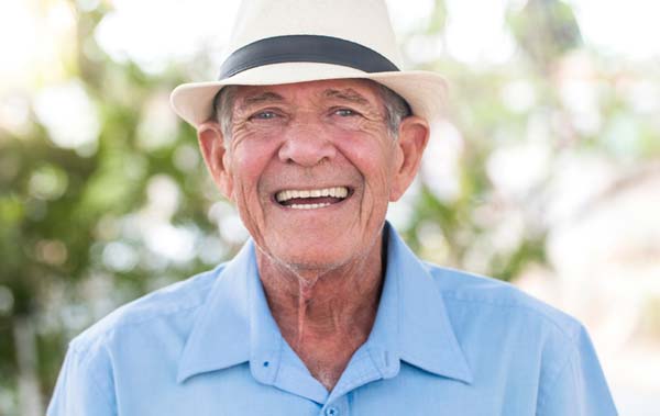 Patient Frank wearing hat and blue shirt smiling in front of trees.