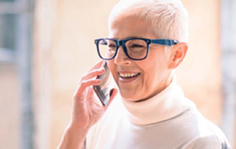 Image of patient talking on phone wearing blue glasses and a white turtleneck.