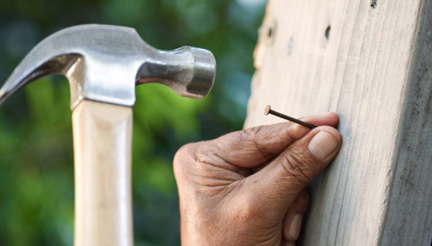 A hand holding a nail and a hammer about to hit the nail.