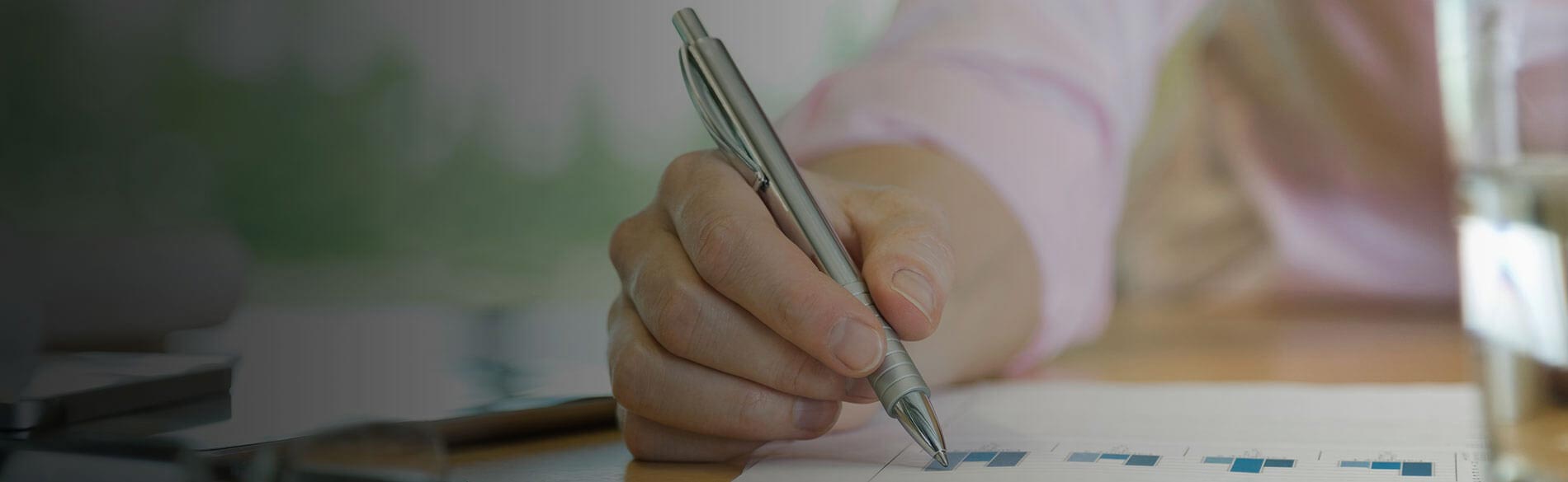 Hand holding a pen over graphs depicted on paper.