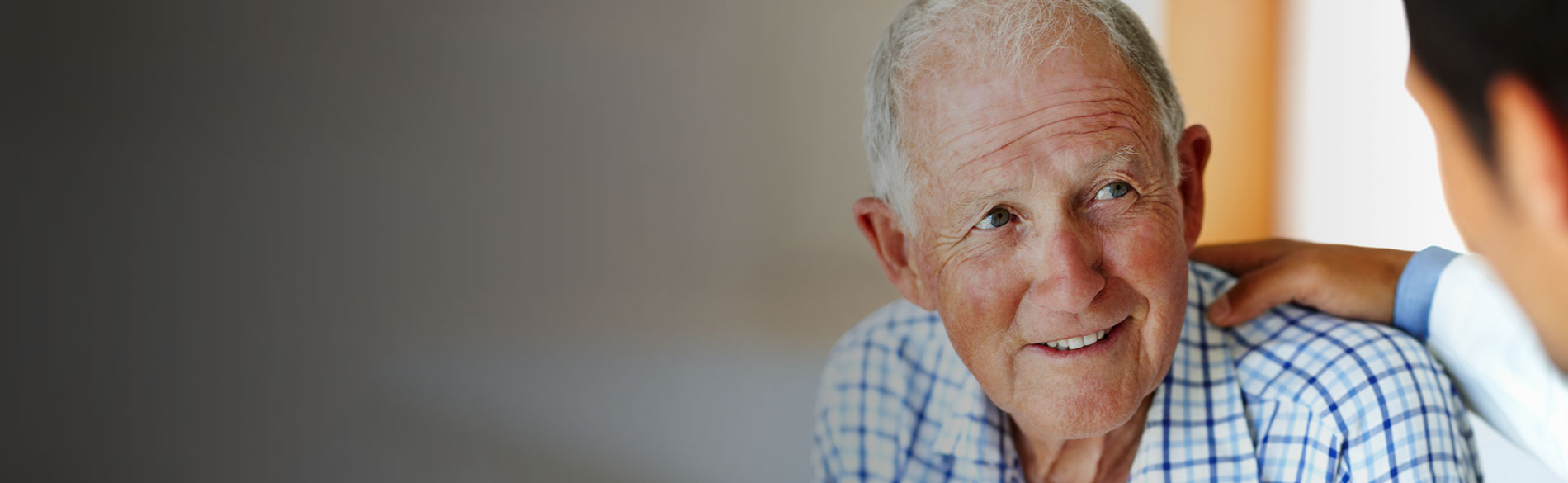 Man in plaid shirt looking at person whose hand is on his shoulder.