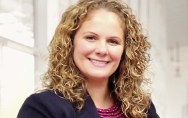 Image of patient education specialist smiling with curly blond hair and wearing a dark blazer.