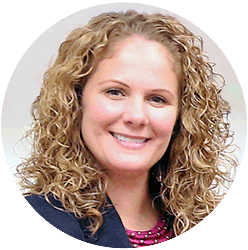 Smiling woman with blond curly hair wearing a blue blazer and pink shirt.