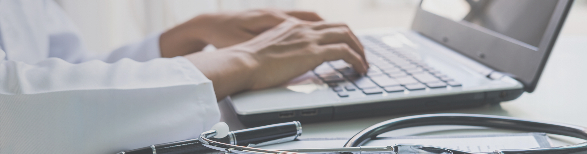 physician typing on laptop with stethoscope on desk