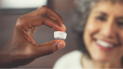 physician hand holding WATCHMAN Device with patient smiling in background