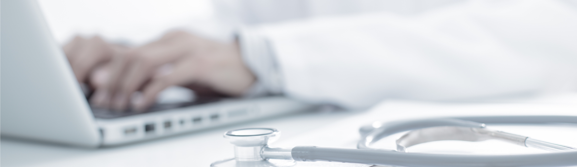 physician typing on laptop with stethoscope on desk