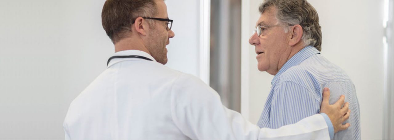 A doctor in a white lab coat speaking with a patient.