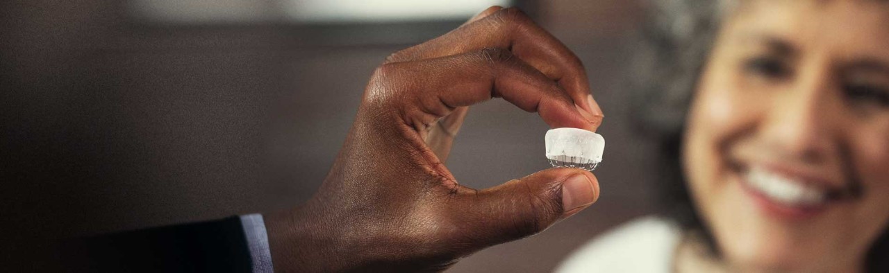 A smiling patient looking at a hand holding the WATCHMAN implant