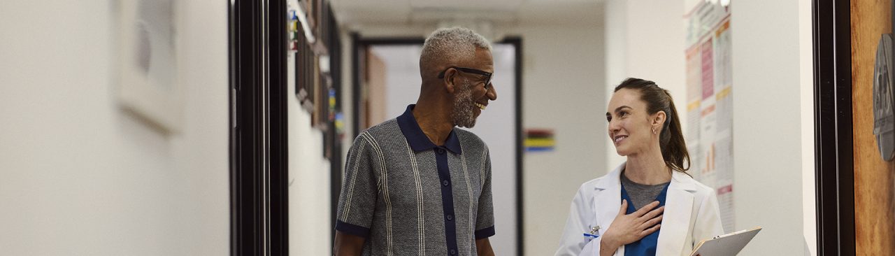 A healthcare professional in white coat speaking with a smiling patient in the hallway of a clinic.