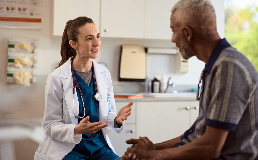 A healthcare professional speaking with a patient in an exam room.