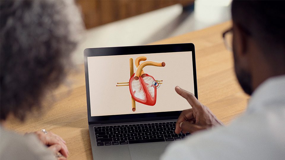 Healthcare provider showing patient diagram of heart on computer screen.