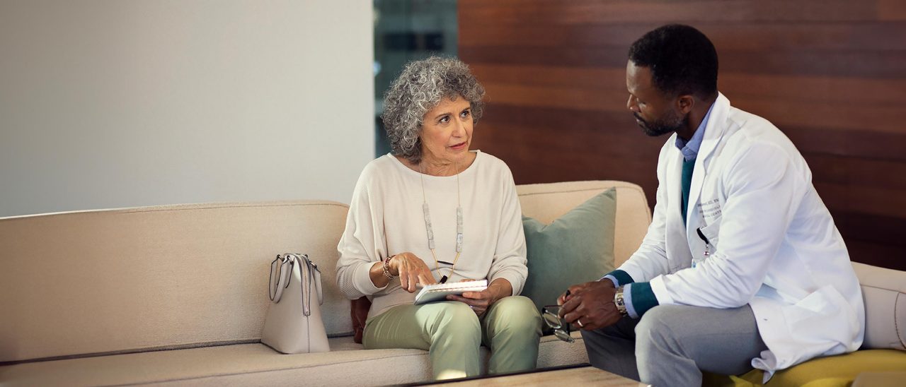 Healthcare provider and patient sitting on a couch and talking.