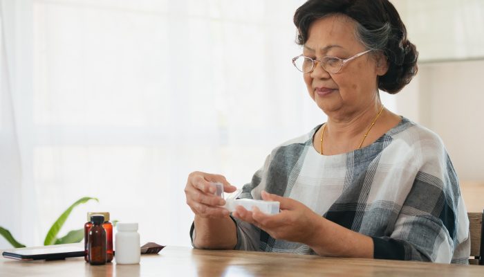 A woman sitting at a table looking at two bottles of pills and reading directions.