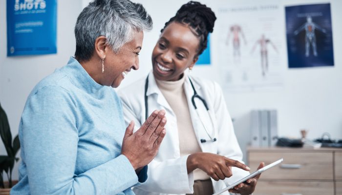 A smiling healthcare professional showing a smiling patient a tablet screen.