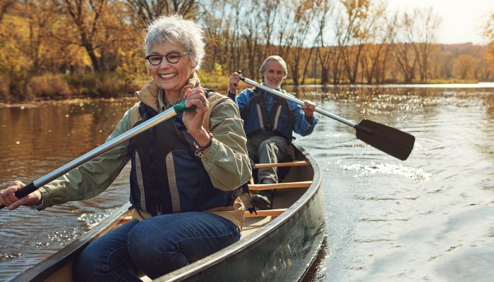 A smiling couple paddling together in a canoe on a river.
