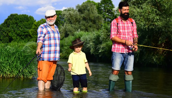 Two men and a little boy standing in a river fishing on a sunny day.