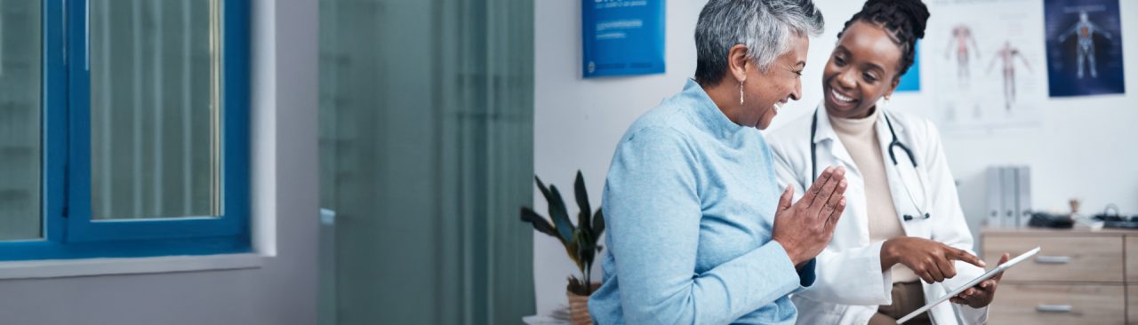 A smiling healthcare professional showing a smiling patient a tablet screen.