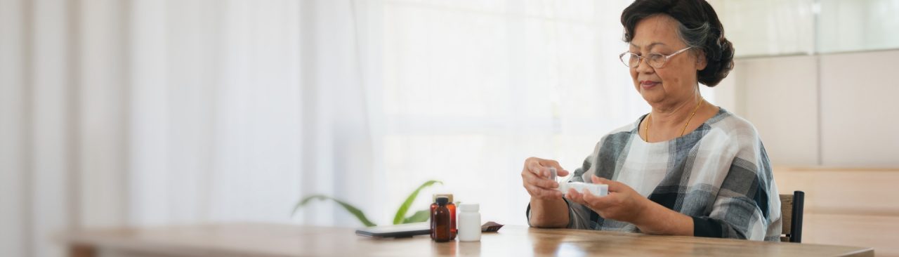 A woman sitting at a table looking at two bottles of pills and reading directions.