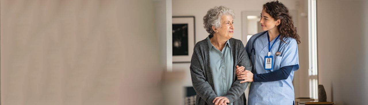 A healthcare professional walking and talking with a patient while supporting their arm.