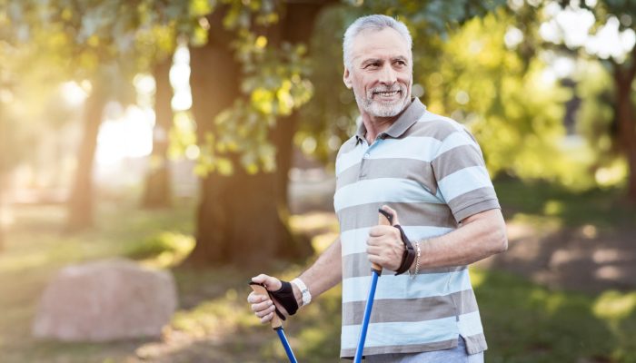 A smiling man exercising outdoors on a sunny day with walking sticks.