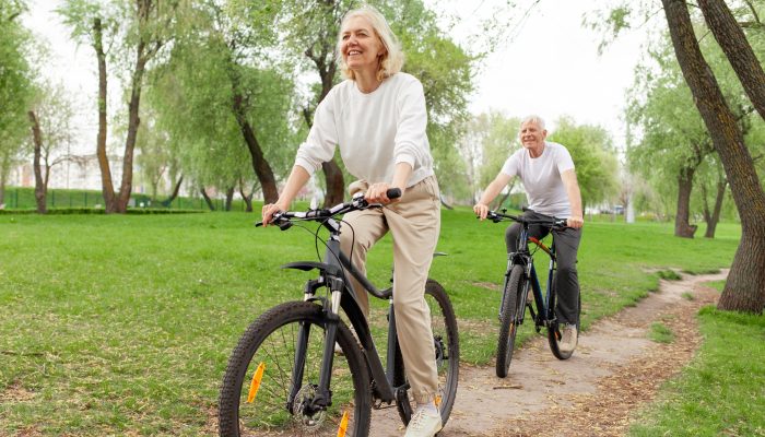 Two smiling people riding bikes along a path outdoors.