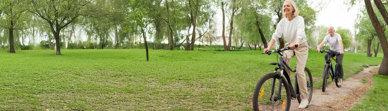 Two smiling people riding bikes along a path outdoors.