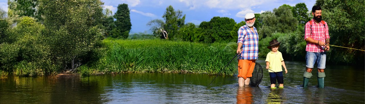 Two men and a little boy standing in a river fishing on a sunny day.