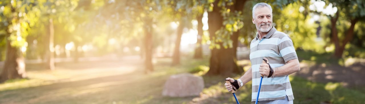 A smiling man exercising outdoors on a sunny day with walking sticks.
