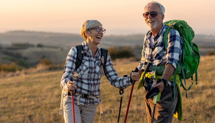 Two smiling people on a hike standing in a grassy field during a sunset.
