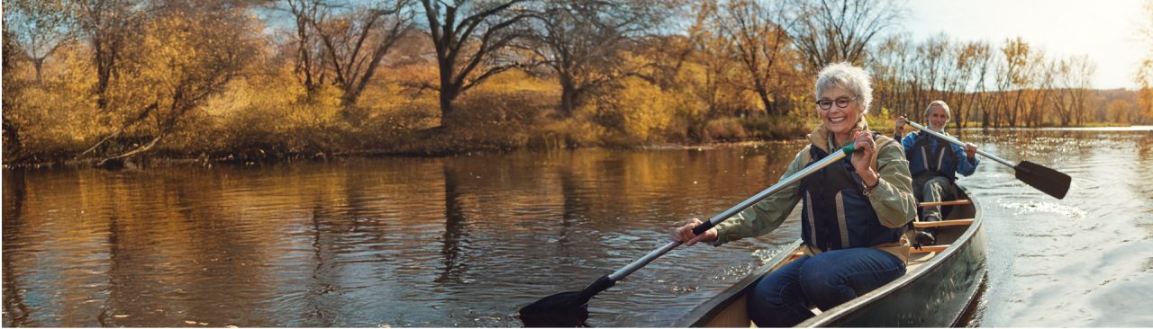 A smiling couple paddling together in a canoe on a river.