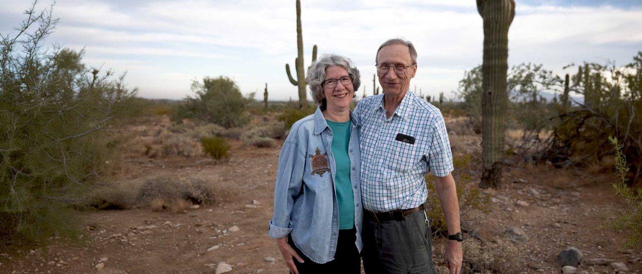 Linda, a WATCHMAN Ambassador, with her husband smiling with the desert behind them.